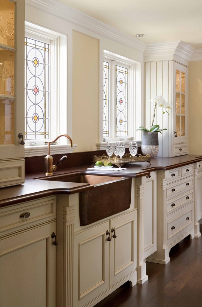 Example of a classic kitchen design in Boston with recessed-panel cabinets, a farmhouse sink, wood countertops, beige cabinets and brown countertops