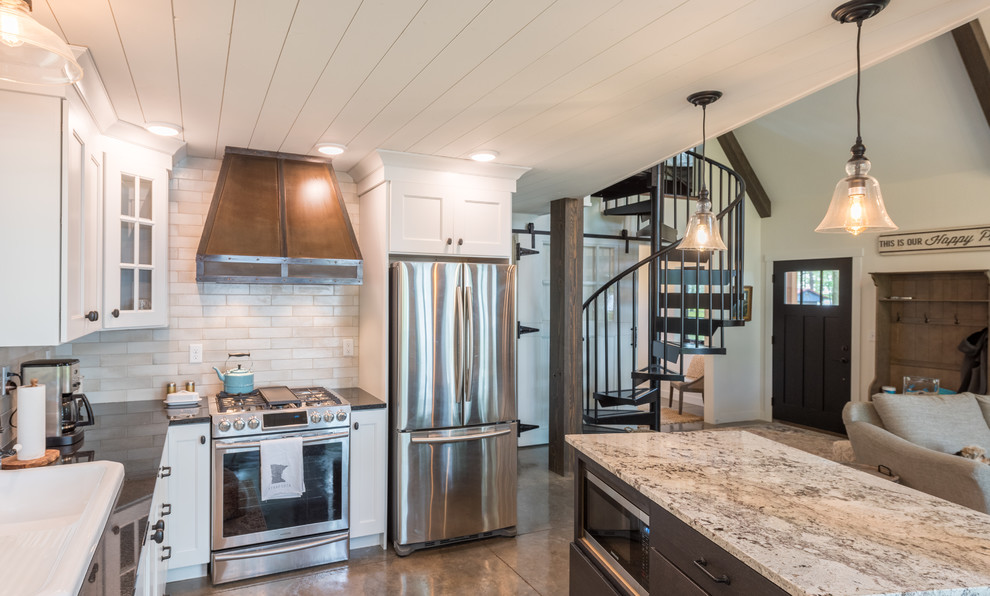 This is an example of a medium sized rustic l-shaped open plan kitchen in Minneapolis with a built-in sink, shaker cabinets, white cabinets, composite countertops, beige splashback, metro tiled splashback, stainless steel appliances, concrete flooring, an island, grey floors and black worktops.