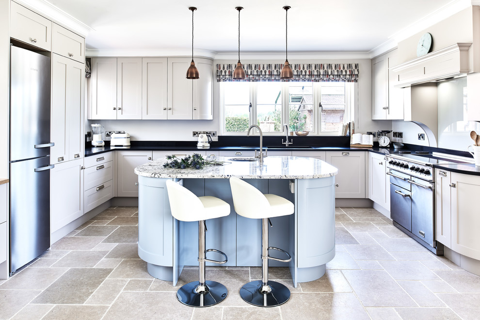 Country u-shaped kitchen in Wiltshire with a submerged sink, shaker cabinets, beige cabinets, stainless steel appliances, an island, grey floors and black worktops.