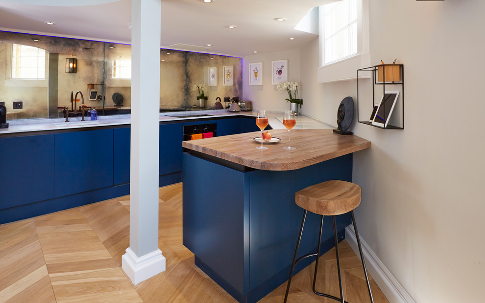 Immagine di una cucina classica di medie dimensioni con ante lisce, ante blu, top in legno, lavello sottopiano, paraspruzzi a specchio, parquet chiaro, penisola e pavimento beige
