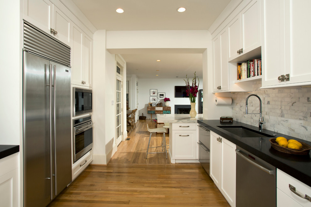 Mid-sized transitional galley light wood floor enclosed kitchen photo in DC Metro with an undermount sink, shaker cabinets, white cabinets, solid surface countertops, gray backsplash, stone tile backsplash, stainless steel appliances and a peninsula