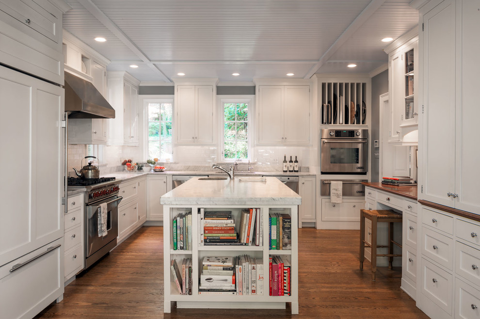 Klassisk inredning av ett u-kök, med en undermonterad diskho, skåp i shakerstil, vita skåp, marmorbänkskiva, vitt stänkskydd, stänkskydd i keramik, integrerade vitvaror, mellanmörkt trägolv, en köksö och brunt golv