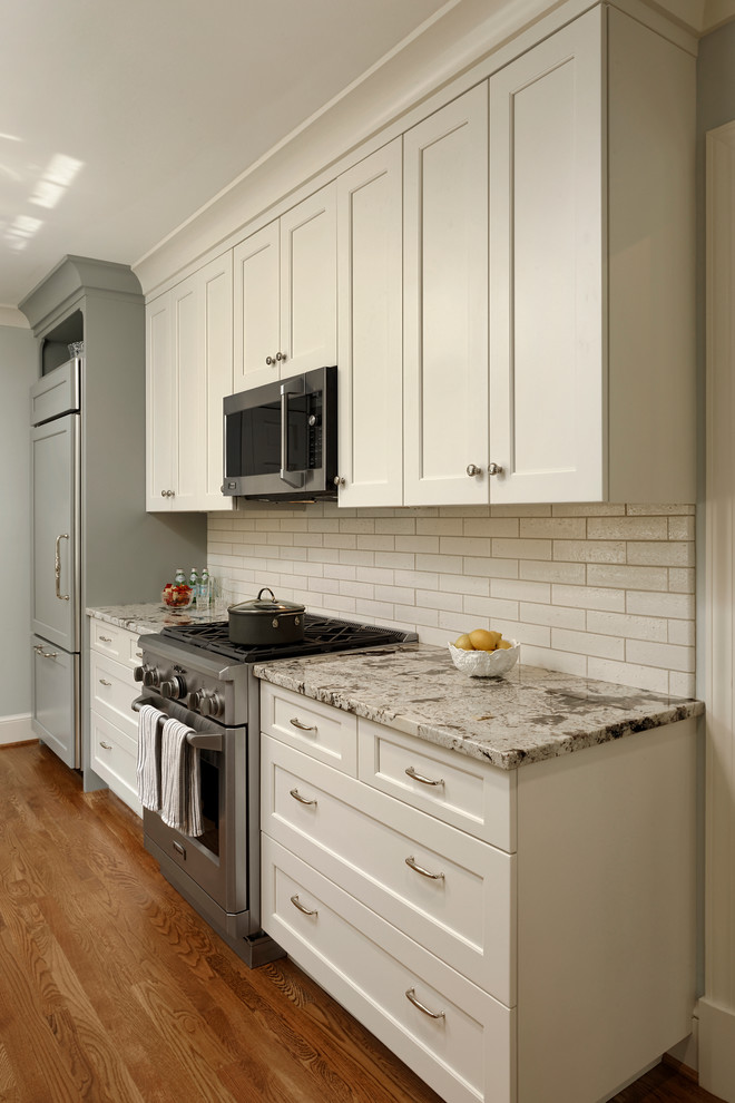 This is an example of a small traditional galley kitchen/diner in DC Metro with a double-bowl sink, glass-front cabinets, white cabinets, granite worktops, white splashback, glass tiled splashback, stainless steel appliances, light hardwood flooring, no island and beige floors.