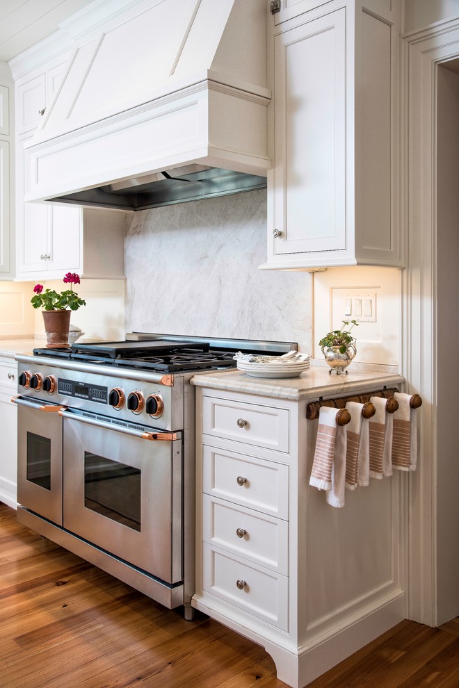 Klassisk inredning av ett stort kök, med en undermonterad diskho, luckor med profilerade fronter, vita skåp, bänkskiva i kalksten, vitt stänkskydd, rostfria vitvaror, mellanmörkt trägolv och en köksö