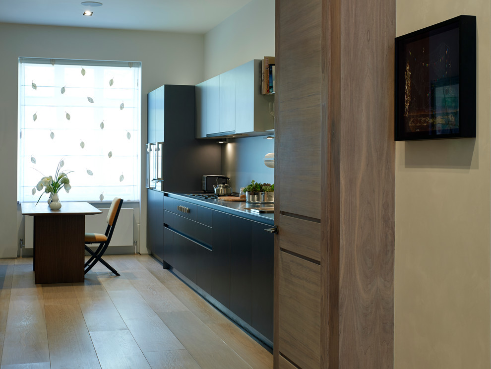 Example of a mid-sized trendy galley light wood floor enclosed kitchen design in London with a drop-in sink, flat-panel cabinets, brown cabinets, stainless steel countertops, metallic backsplash, metal backsplash and paneled appliances