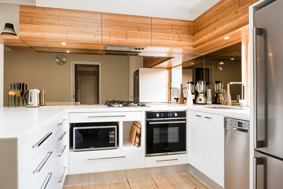 Kleine Moderne Wohnküche ohne Insel in U-Form mit Doppelwaschbecken, weißen Schränken, Mineralwerkstoff-Arbeitsplatte, Rückwand aus Spiegelfliesen und Küchengeräten aus Edelstahl in Melbourne