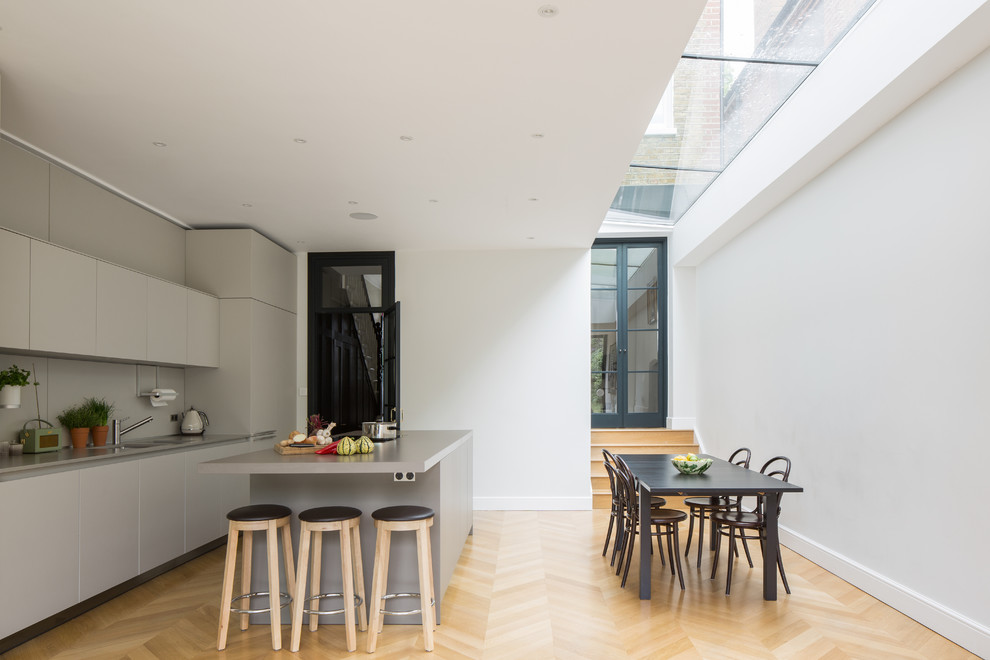 Einzeilige, Mittelgroße Moderne Wohnküche mit flächenbündigen Schrankfronten, grauen Schränken, Küchenrückwand in Grau, Elektrogeräten mit Frontblende, hellem Holzboden, Halbinsel und beigem Boden in London