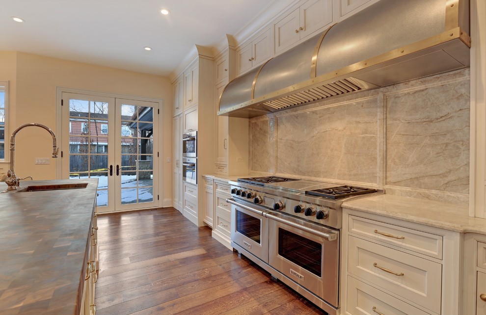 Example of a large classic u-shaped medium tone wood floor open concept kitchen design in Chicago with an undermount sink, recessed-panel cabinets, white cabinets, wood countertops, gray backsplash, stone slab backsplash, stainless steel appliances and an island