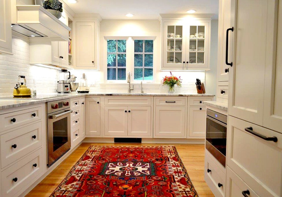 Bild på ett litet lantligt kök, med en enkel diskho, luckor med infälld panel, vita skåp, marmorbänkskiva, vitt stänkskydd, stänkskydd i tunnelbanekakel, rostfria vitvaror, ljust trägolv och beiget golv