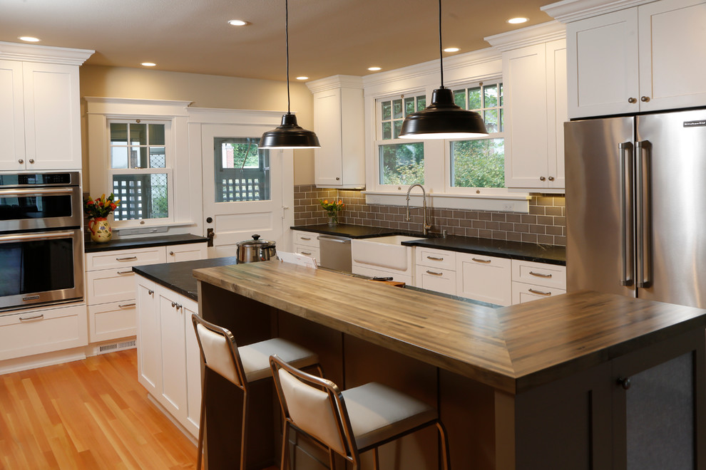 Bild på ett amerikanskt kök och matrum, med en rustik diskho, skåp i shakerstil, vita skåp, bänkskiva i koppar, brunt stänkskydd, stänkskydd i tunnelbanekakel, rostfria vitvaror, ljust trägolv och en köksö