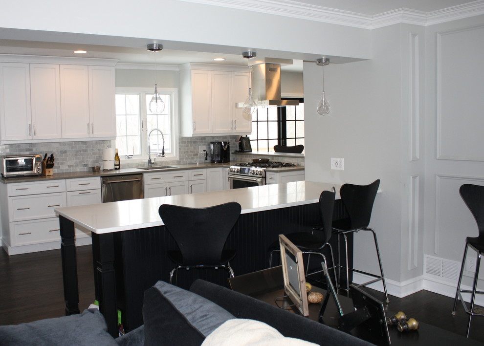 Modern inredning av ett kök, med en undermonterad diskho, luckor med infälld panel, vita skåp, grått stänkskydd, rostfria vitvaror, mörkt trägolv och en halv köksö