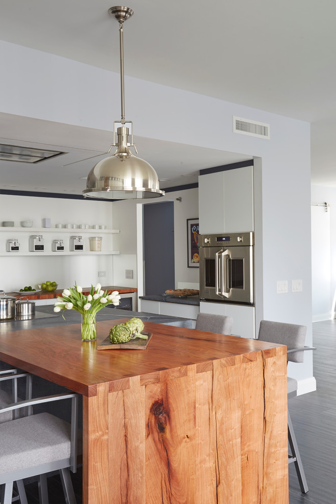 Large contemporary u-shaped kitchen/diner in Chicago with a single-bowl sink, glass-front cabinets, white cabinets, soapstone worktops, metallic splashback, mirror splashback, stainless steel appliances, cork flooring and an island.