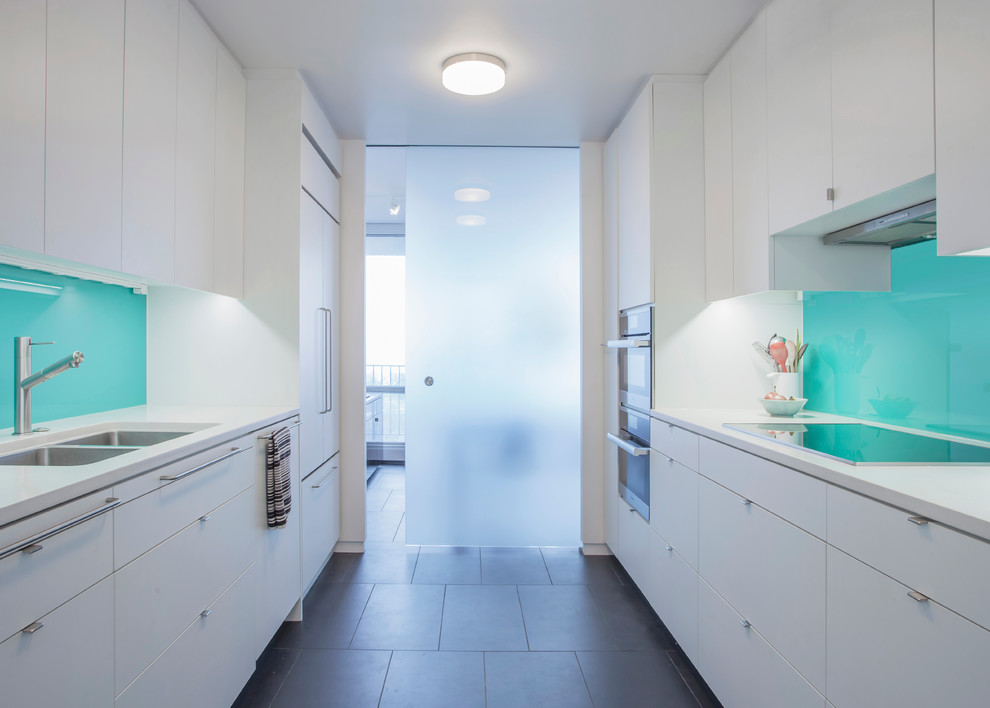 Zweizeilige Moderne Küche mit flächenbündigen Schrankfronten, weißen Schränken, Quarzwerkstein-Arbeitsplatte, Küchenrückwand in Blau, Glasrückwand und Küchengeräten aus Edelstahl in Chicago