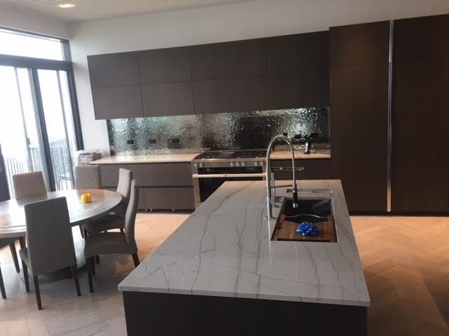 This is an example of a large modern l-shaped open plan kitchen in Orange County with a submerged sink, flat-panel cabinets, black cabinets, quartz worktops, metallic splashback, metal splashback, stainless steel appliances, limestone flooring and an island.