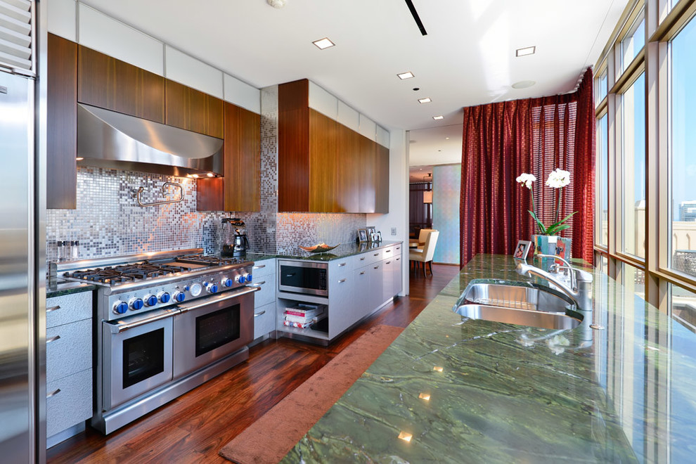 Exempel på ett avskilt modernt linjärt kök, med en undermonterad diskho, släta luckor, skåp i rostfritt stål, granitbänkskiva, stänkskydd med metallisk yta, stänkskydd i metallkakel, rostfria vitvaror, laminatgolv och brunt golv