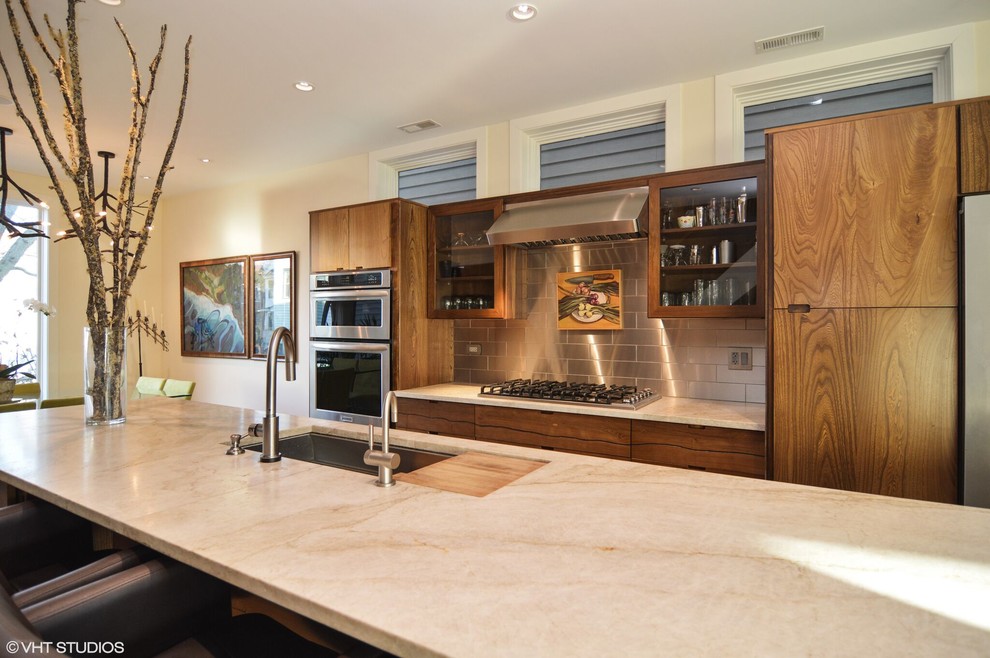 Inredning av ett modernt kök och matrum, med luckor med glaspanel, stänkskydd med metallisk yta, rostfria vitvaror och en köksö