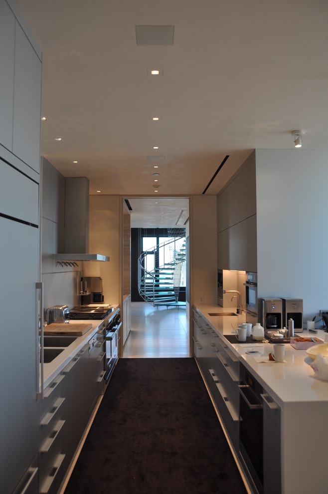 Photo of a large contemporary galley enclosed kitchen in Chicago with stainless steel appliances, a double-bowl sink, flat-panel cabinets, grey cabinets, composite countertops, no island, carpet and black floors.