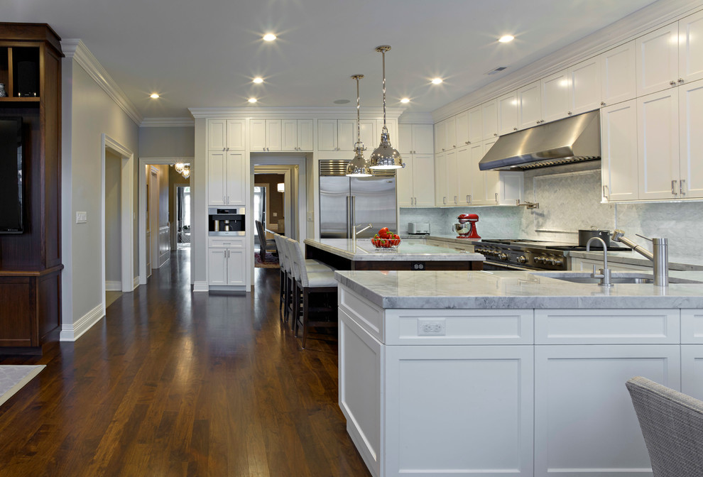 Inredning av ett klassiskt stort kök, med en undermonterad diskho, luckor med infälld panel, vita skåp, grått stänkskydd, stänkskydd i stenkakel, rostfria vitvaror, mörkt trägolv och en köksö