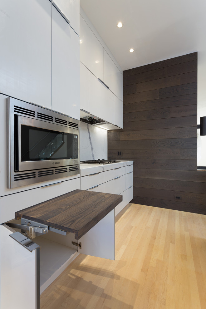 Example of a large minimalist single-wall light wood floor open concept kitchen design in Chicago with a farmhouse sink, flat-panel cabinets, white cabinets, marble countertops, white backsplash, porcelain backsplash, stainless steel appliances and an island