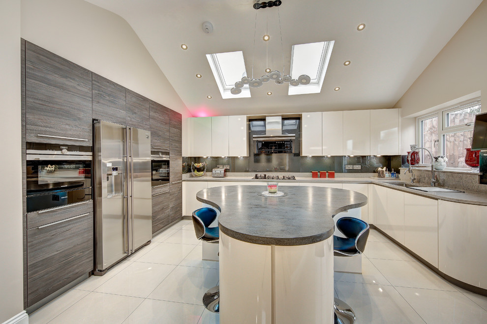 Modern inredning av ett stort u-kök, med en köksö, släta luckor, vita skåp, grått stänkskydd, rostfria vitvaror och vitt golv