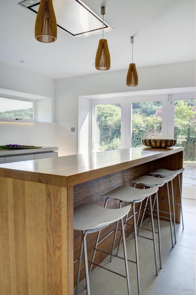 Inspiration for an expansive contemporary single-wall open plan kitchen in London with an integrated sink, flat-panel cabinets, white cabinets, concrete worktops, cement flooring, a breakfast bar, grey floors and grey worktops.