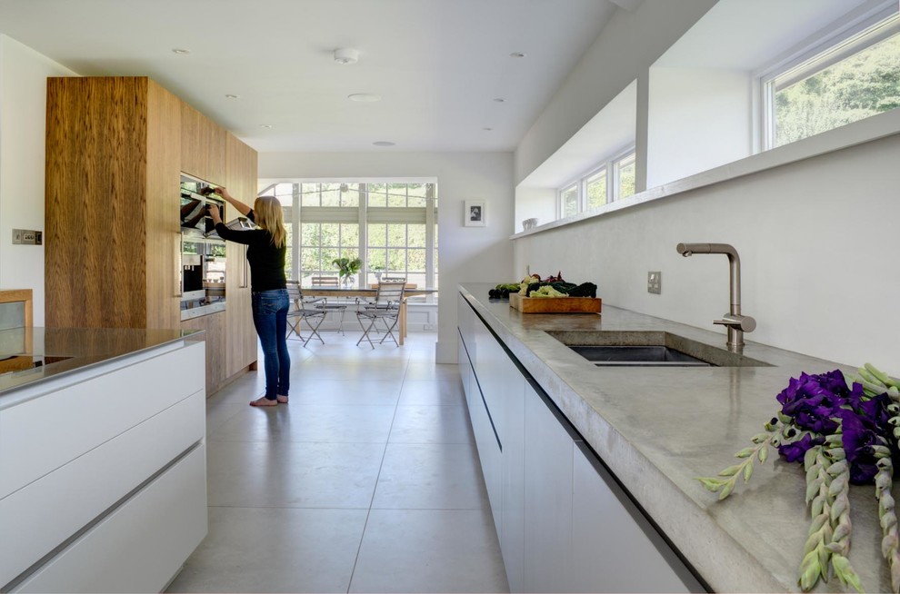Идея дизайна: огромная прямая кухня-гостиная в современном стиле с монолитной мойкой, плоскими фасадами, белыми фасадами, столешницей из бетона, полом из цементной плитки, полуостровом, серым полом и серой столешницей