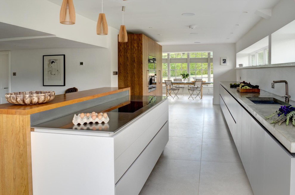 Expansive contemporary single-wall open plan kitchen in London with an integrated sink, flat-panel cabinets, white cabinets, concrete worktops, cement flooring, a breakfast bar, grey floors and grey worktops.