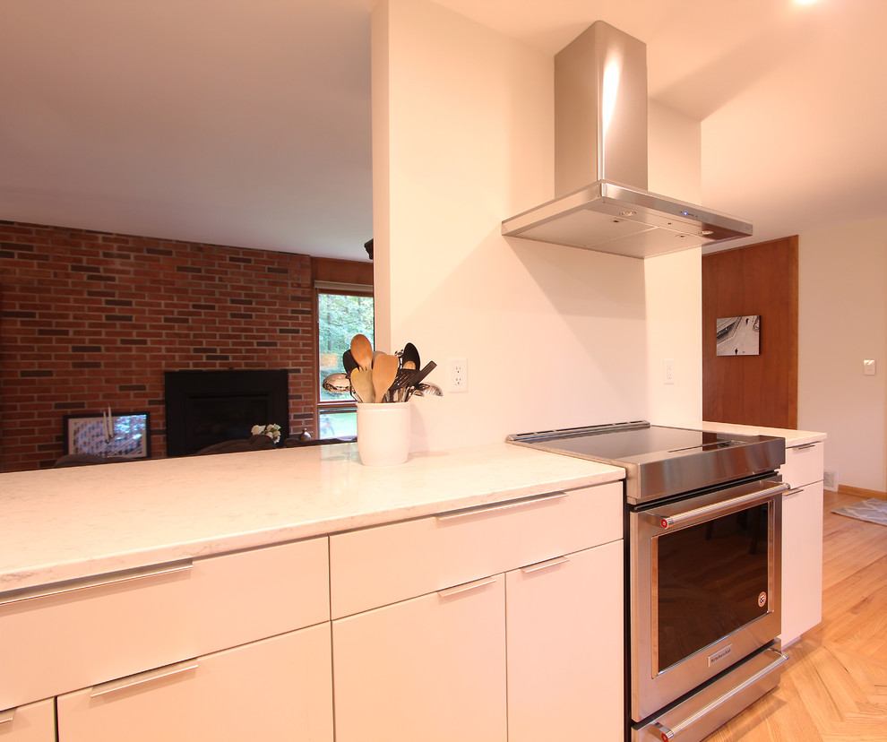 This is an example of a medium sized modern u-shaped kitchen/diner in Other with a submerged sink, flat-panel cabinets, white cabinets, engineered stone countertops, stone slab splashback, medium hardwood flooring, brown floors, white splashback, black appliances, an island and white worktops.