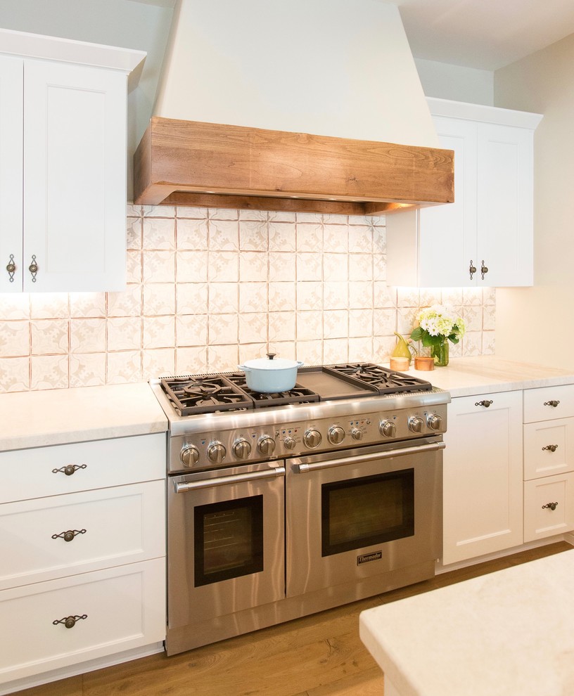 Exempel på ett stort medelhavsstil kök, med en undermonterad diskho, luckor med infälld panel, vita skåp, bänkskiva i kvartsit, stänkskydd i keramik, rostfria vitvaror, mellanmörkt trägolv och en köksö