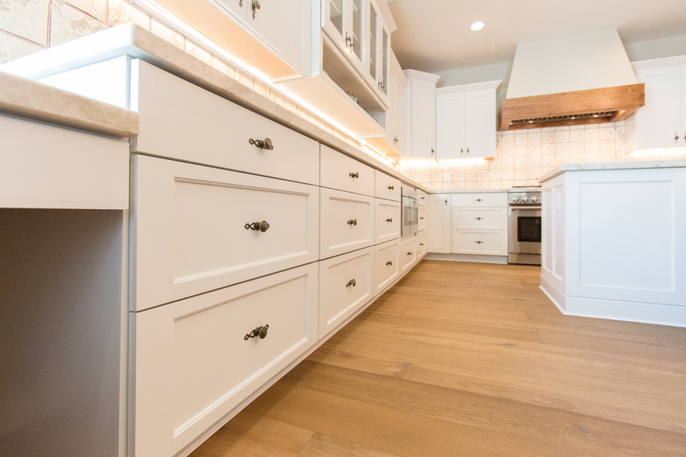 Bild på ett stort medelhavsstil kök, med en undermonterad diskho, luckor med infälld panel, vita skåp, bänkskiva i kvartsit, stänkskydd i keramik, rostfria vitvaror, mellanmörkt trägolv och en köksö