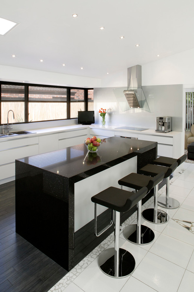 На фото: кухня в современном стиле с плоскими фасадами, белыми фасадами, серым фартуком, фартуком из стекла, островом и черной столешницей