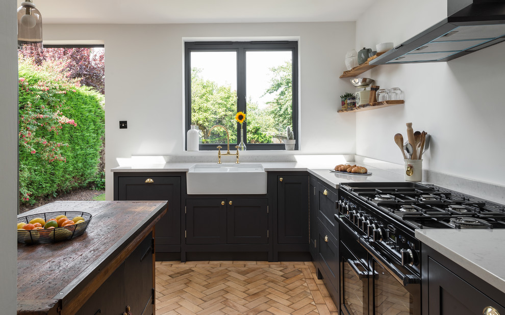Medium sized classic open plan kitchen in London with shaker cabinets, quartz worktops, medium hardwood flooring, an island, a belfast sink, white splashback, black appliances and brown floors.