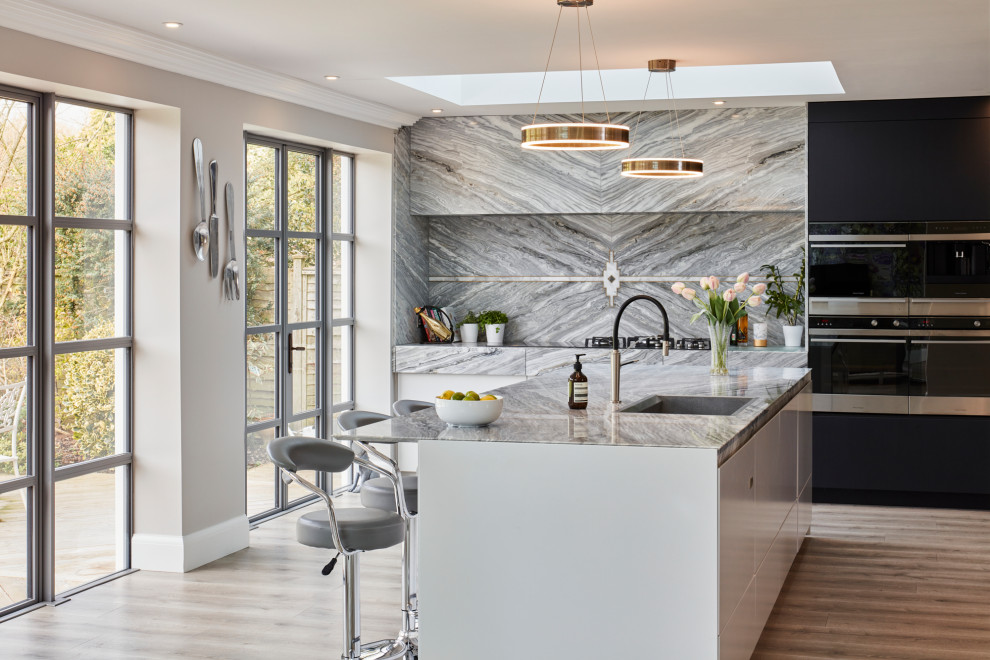 Photo of a large contemporary l-shaped open plan kitchen in Kent with flat-panel cabinets, grey splashback, marble splashback, stainless steel appliances, an island, grey floors and grey worktops.