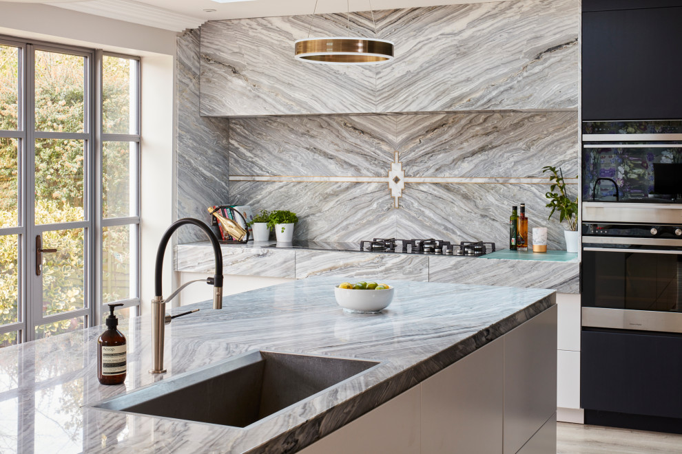 Bild på ett stort funkis grå grått kök, med släta luckor, grått stänkskydd, stänkskydd i marmor, rostfria vitvaror, en köksö och grått golv
