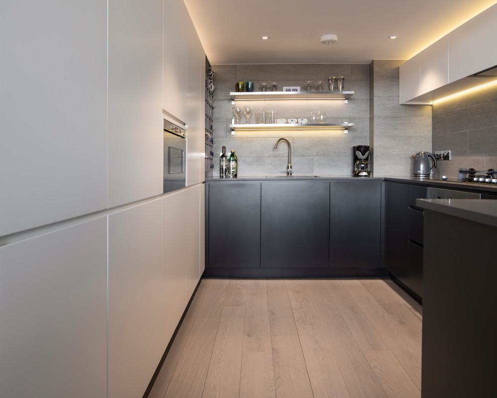 Inspiration for a small urban u-shaped open plan kitchen in London with a built-in sink, flat-panel cabinets, grey cabinets, engineered stone countertops, grey splashback, ceramic splashback, integrated appliances, light hardwood flooring and a breakfast bar.