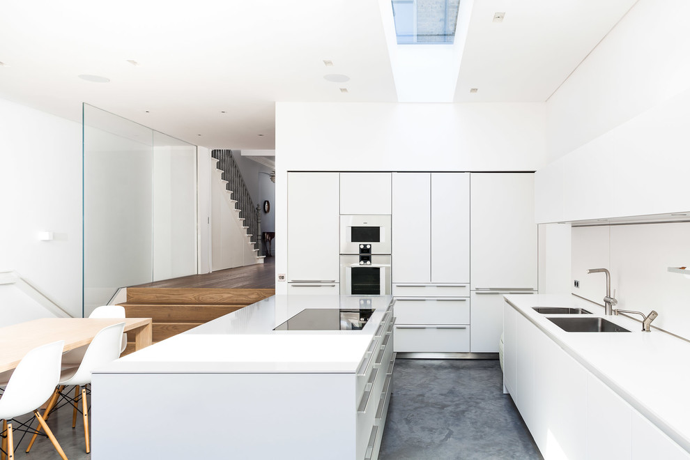 Inspiration for a contemporary kitchen/diner in London with a double-bowl sink, flat-panel cabinets, white cabinets, white splashback, concrete flooring and an island.