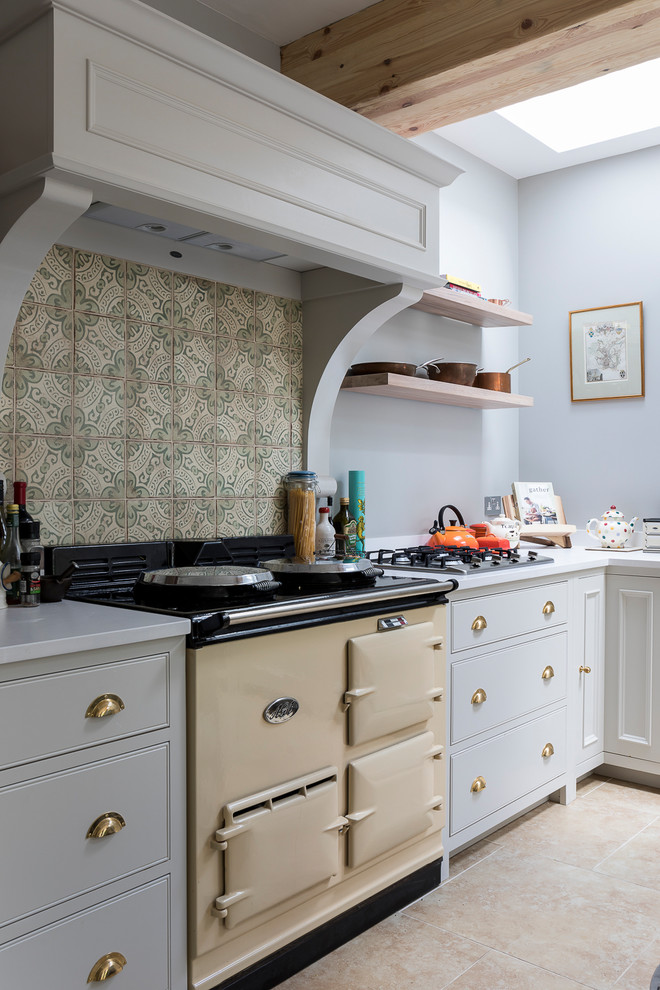 This is an example of a medium sized country l-shaped kitchen/diner in London with a belfast sink, shaker cabinets, grey cabinets, composite countertops, green splashback, porcelain splashback, stainless steel appliances, limestone flooring, an island and beige floors.