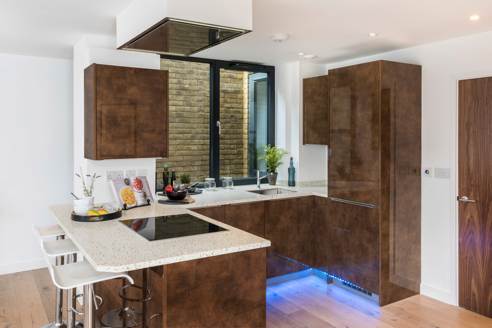 Contemporary u-shaped kitchen in London with a submerged sink, flat-panel cabinets, brown cabinets, light hardwood flooring, a breakfast bar, brown floors and beige worktops.