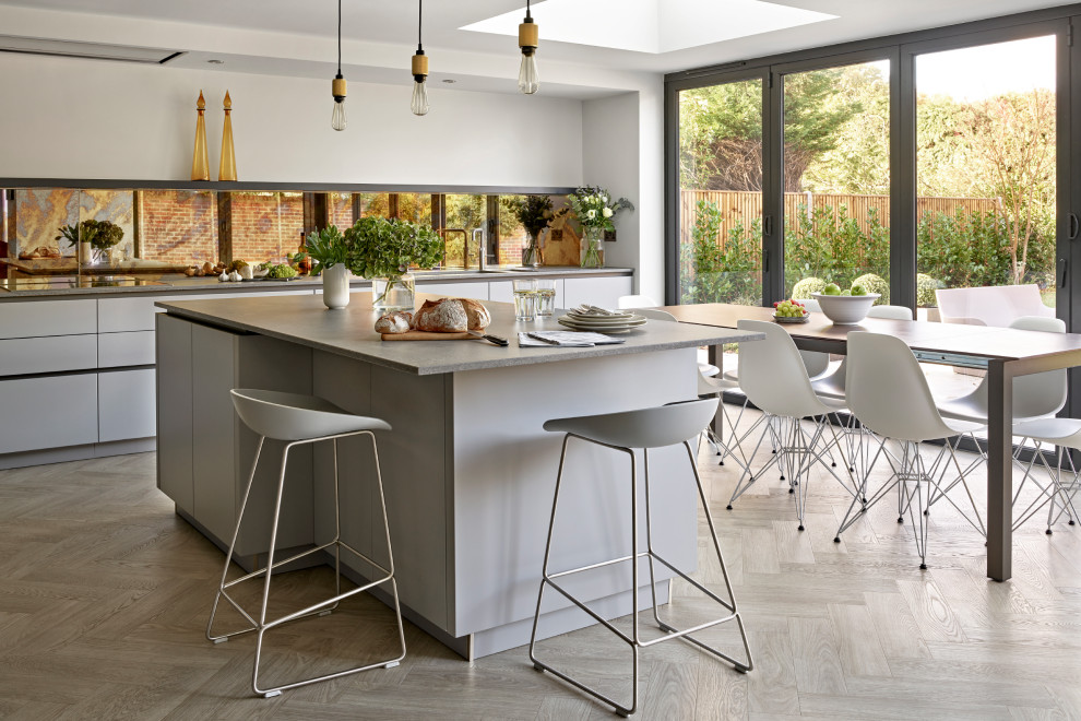 Modern inredning av ett stort grå grått kök, med en undermonterad diskho, släta luckor, grå skåp, bänkskiva i kvartsit, stänkskydd med metallisk yta, spegel som stänkskydd, vinylgolv, en köksö och beiget golv