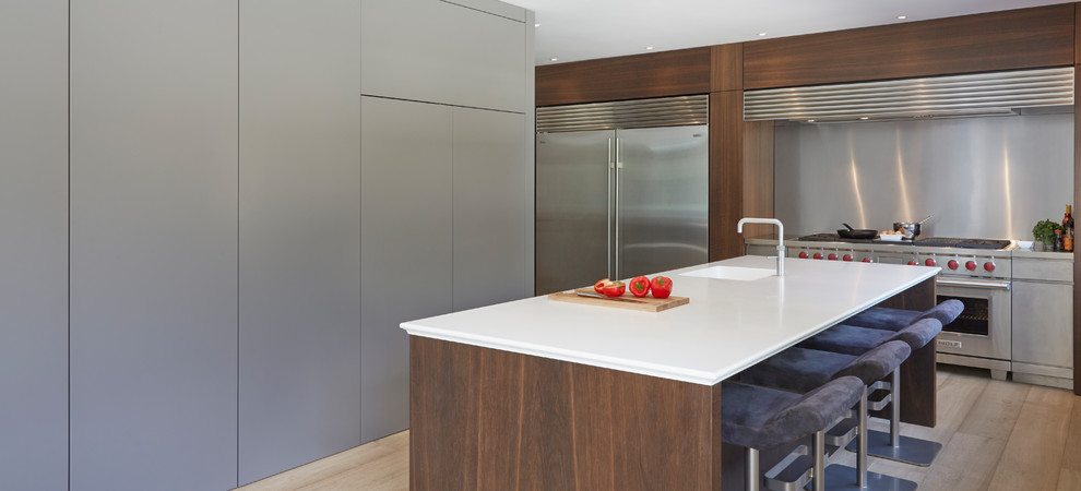 Photo of a modern kitchen in Other with an integrated sink, flat-panel cabinets, grey cabinets, composite countertops, metallic splashback, stainless steel appliances, medium hardwood flooring and a breakfast bar.