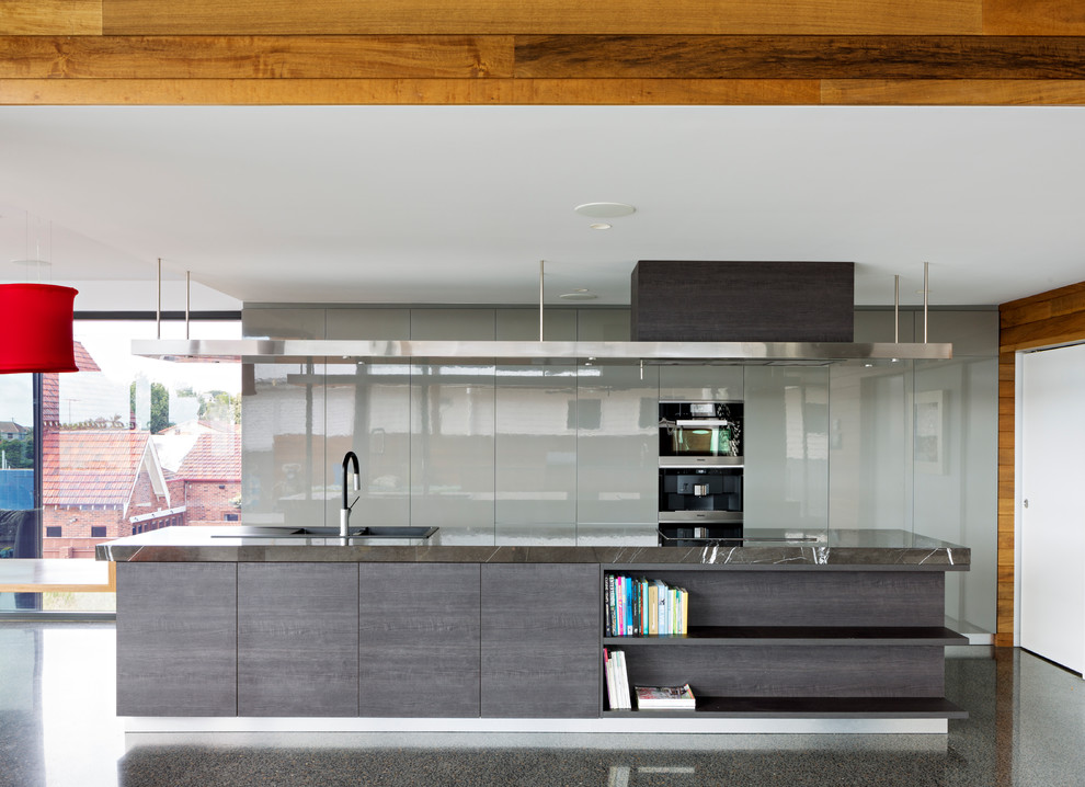Inspiration for a contemporary galley open plan kitchen in Brisbane with a built-in sink, flat-panel cabinets, grey cabinets, black appliances, concrete flooring, an island, grey floors and grey worktops.