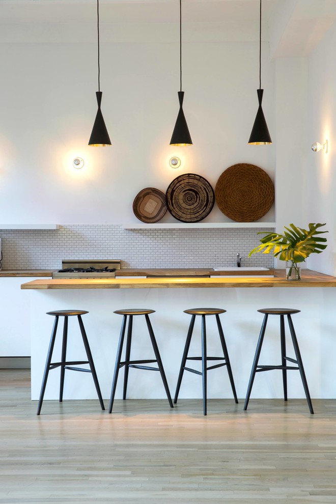 Open concept kitchen - large contemporary u-shaped light wood floor and beige floor open concept kitchen idea in New York with wood countertops, flat-panel cabinets, white backsplash, subway tile backsplash, paneled appliances, a peninsula, a drop-in sink, white cabinets and brown countertops