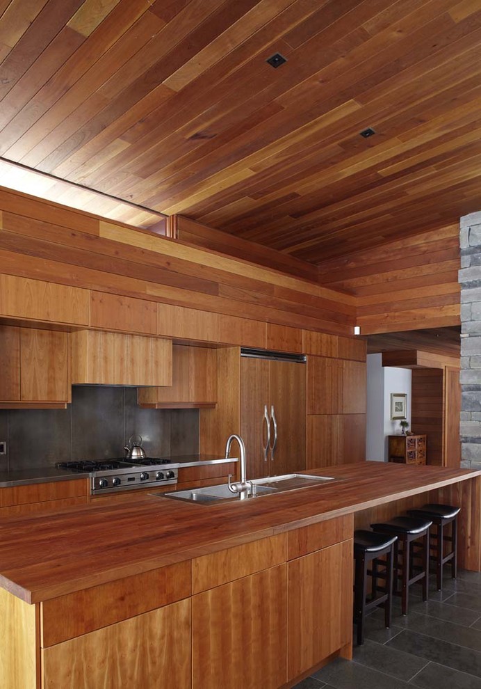 На фото: большая параллельная кухня-гостиная в современном стиле с плоскими фасадами, техникой под мебельный фасад, деревянной столешницей, накладной мойкой, фасадами цвета дерева среднего тона, серым фартуком, полом из керамической плитки и островом