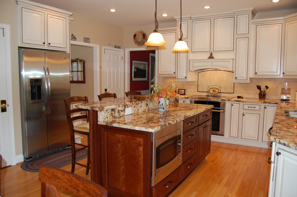 Mid-sized elegant l-shaped light wood floor and brown floor enclosed kitchen photo in Philadelphia with a double-bowl sink, raised-panel cabinets, white cabinets, granite countertops, beige backsplash, stone tile backsplash, paneled appliances and an island