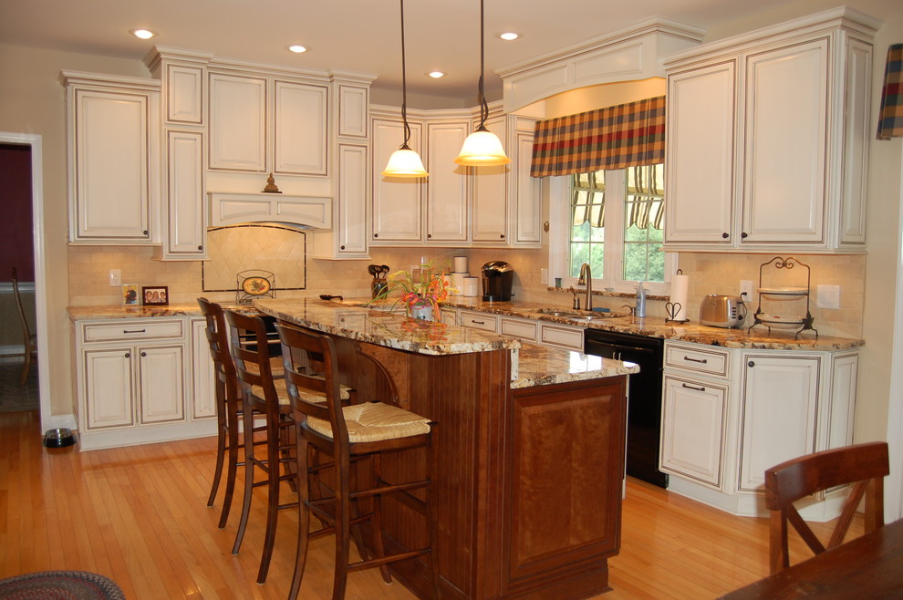 Inspiration for a mid-sized timeless l-shaped light wood floor and brown floor enclosed kitchen remodel in Philadelphia with a double-bowl sink, raised-panel cabinets, white cabinets, granite countertops, beige backsplash, stone tile backsplash, paneled appliances and an island