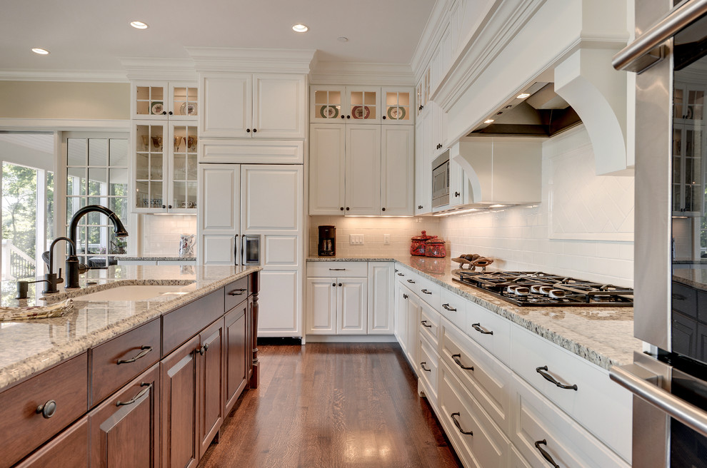 Cette photo montre une cuisine américaine tendance avec des portes de placard blanches, une crédence blanche, un électroménager en acier inoxydable, un sol en bois brun et îlot.