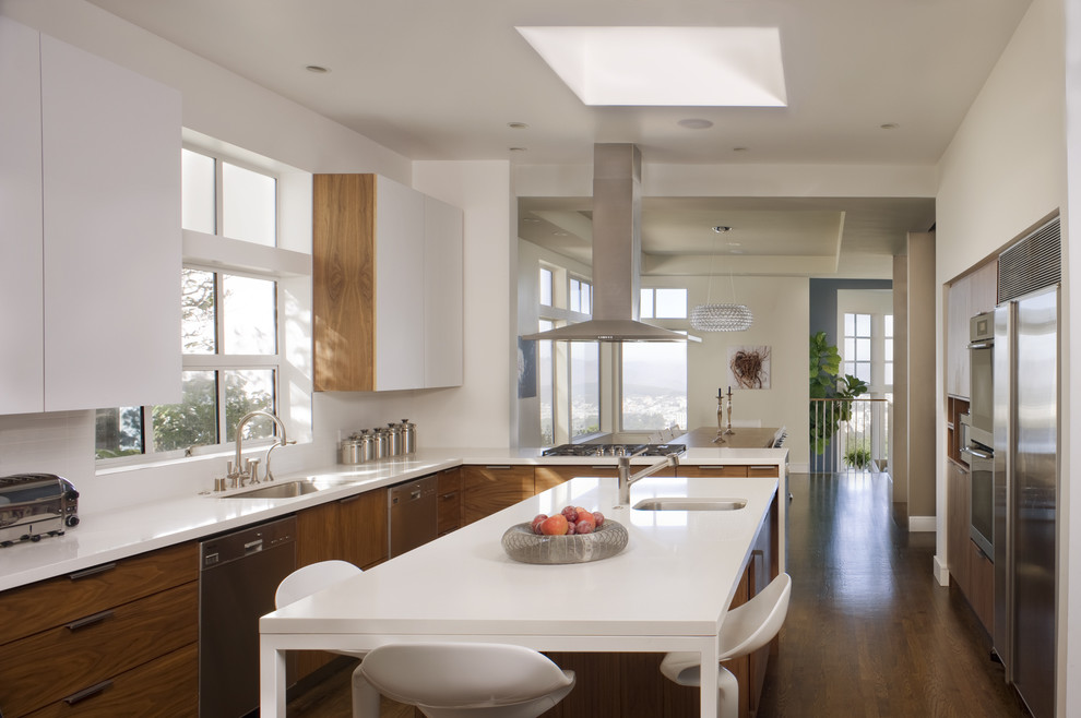 Imagen de cocina contemporánea con electrodomésticos de acero inoxidable, fregadero bajoencimera, armarios con paneles lisos, puertas de armario de madera oscura y barras de cocina