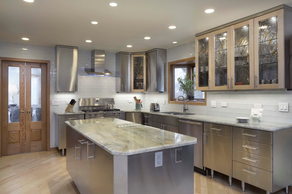 Medium sized contemporary kitchen/diner in Chicago with a submerged sink, flat-panel cabinets, stainless steel cabinets, marble worktops, white splashback, metro tiled splashback, stainless steel appliances, light hardwood flooring and an island.