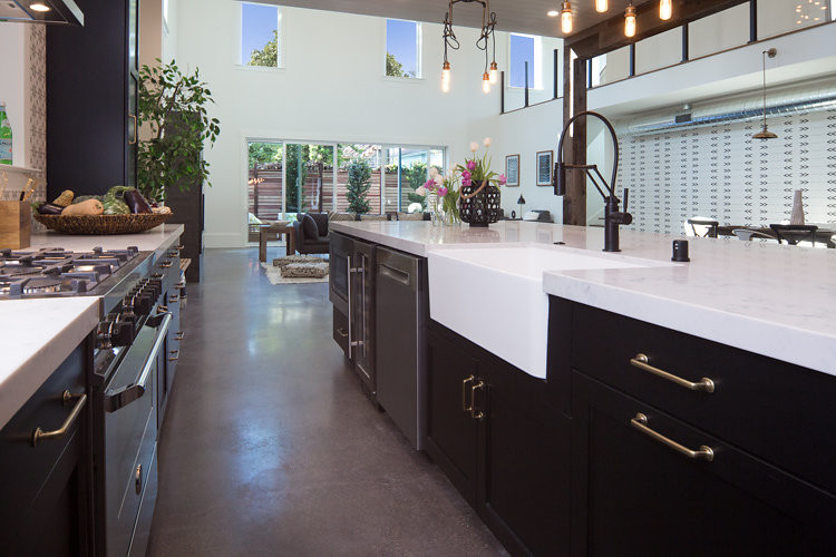 Inspiration for a large industrial single-wall concrete floor eat-in kitchen remodel in San Francisco with a double-bowl sink, shaker cabinets, black cabinets, solid surface countertops, beige backsplash, stainless steel appliances and an island