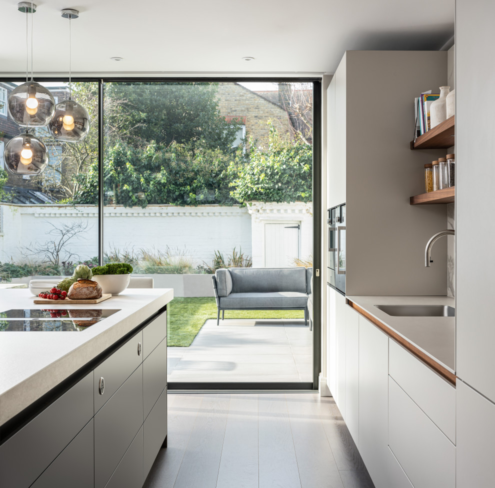 This is an example of a large contemporary galley kitchen in London with a submerged sink, flat-panel cabinets, white cabinets, integrated appliances, porcelain flooring, an island, grey floors and grey worktops.